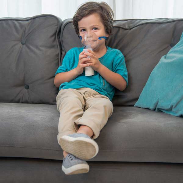 Omron MicroAir U100 Nebuliser young boy using nebuliser sitting upright on sofa